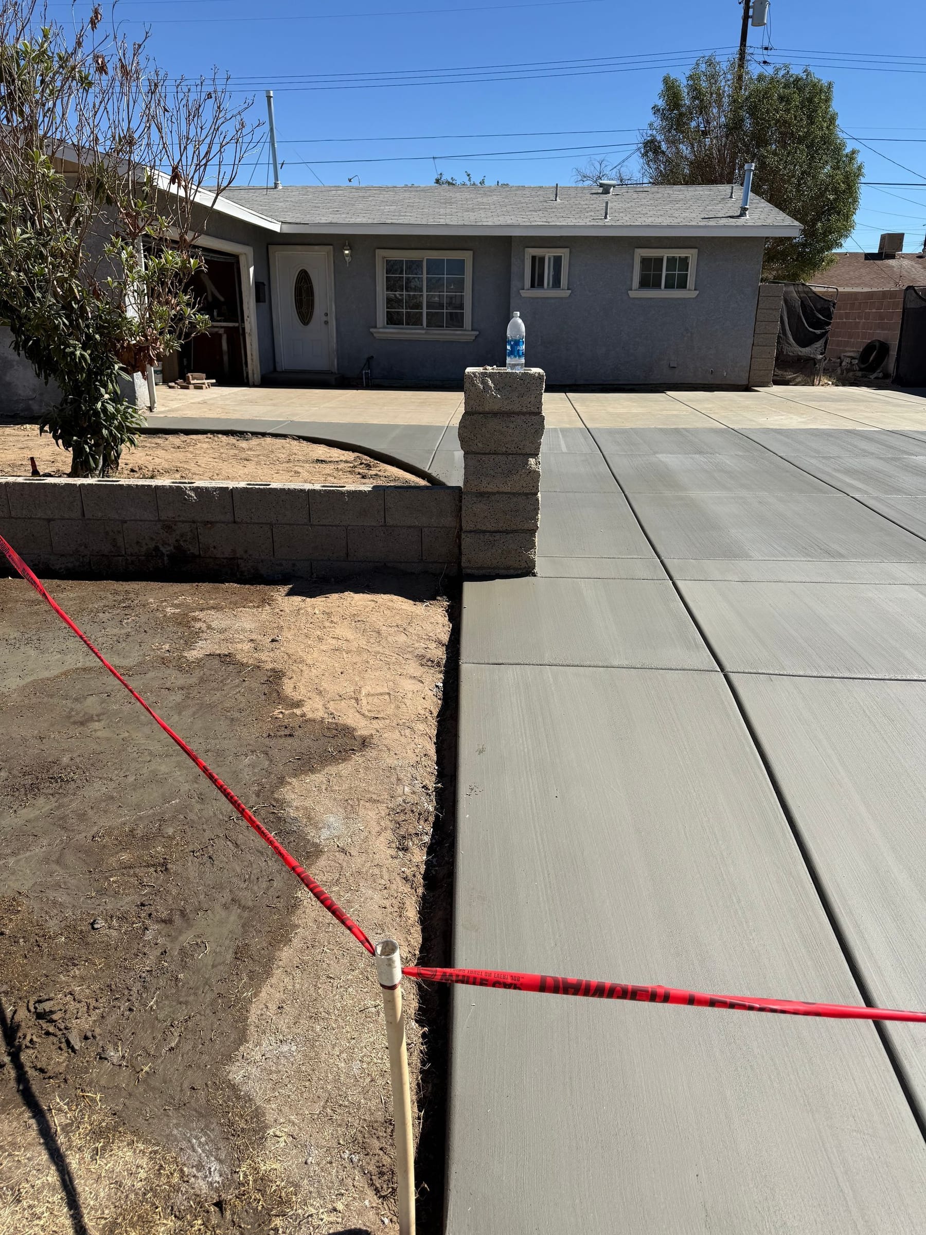 Newly poured concrete driveway and sidewalk with house in the background. 