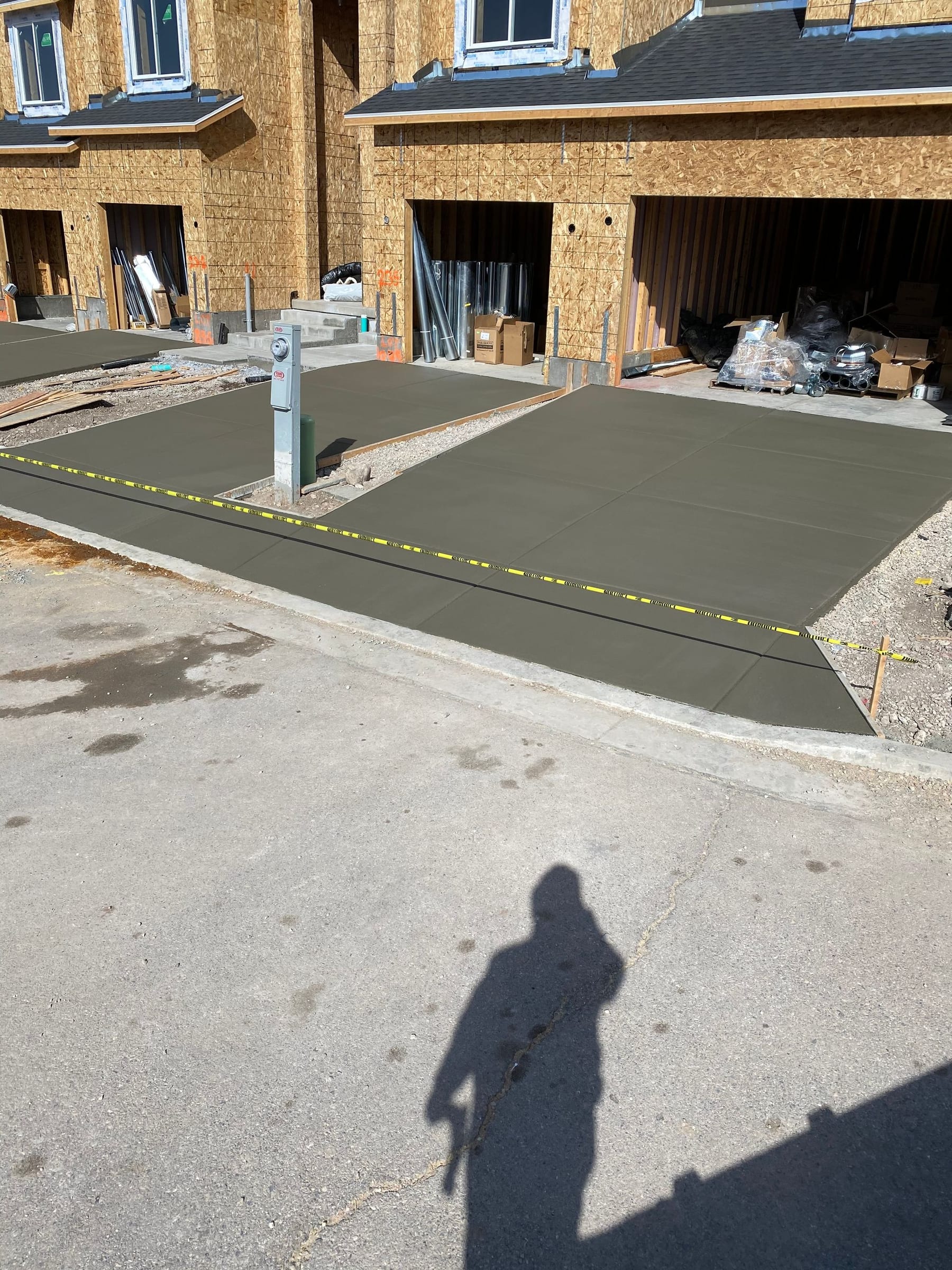 Concrete driveway under construction in front of townhouses, with a person's shadow in the foreground.